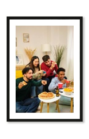 Group of multiethnic friends eating pizza and playing video games in shared apartment.