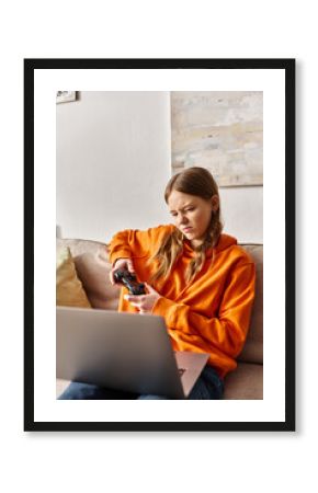 displeased teenage girl gaming with joystick and laptop while sitting on sofa at home, entertainment