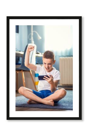 Boy playing video game on smartphone sitting on floor in his room.