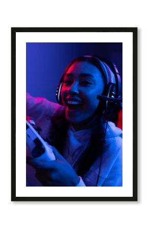 Happy biracial woman wearing headphones playing video games with controller