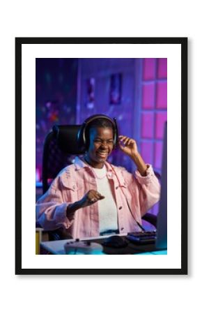 Vertical portrait of emotional Black young woman playing video games at night and celebrating victory with neon lighting