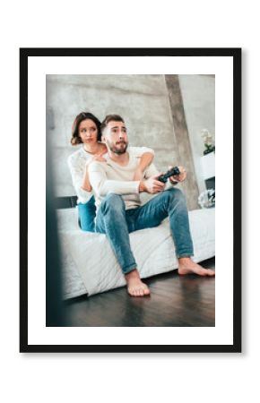 low angle view of brunette woman hugging handsome man sitting on bed and playing video game