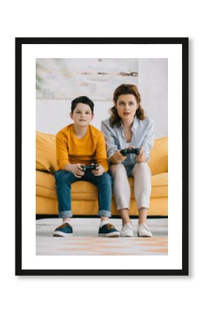 attentive mother and son holding joysticks and playing video game at home