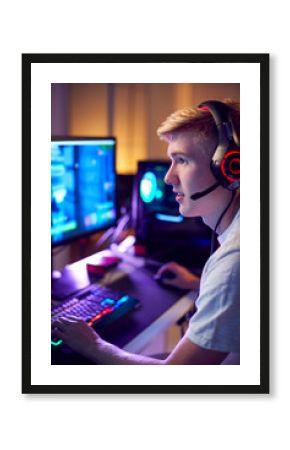 Teenage Boy Wearing Headset Gaming At Home Using Dual Computer Screens