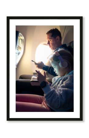 Young girl engaged with a screen, sitting with her dad on an airplane