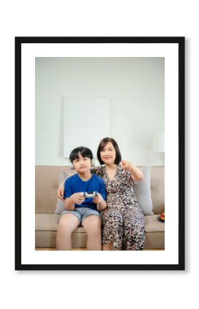 Mother and son sitting together on the couch playing computer game in room