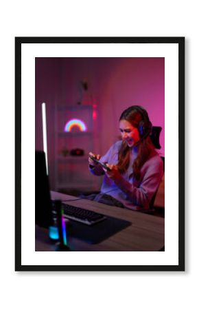 Asian young adult woman gamer plays mobile game intensely headset neon light gaming room