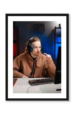 Male gamer in headphones showing small size with fingers gesture measure, play video game online in neon light at night. Gaming Home. Online Multiplayer Championship. Esport streaming game.