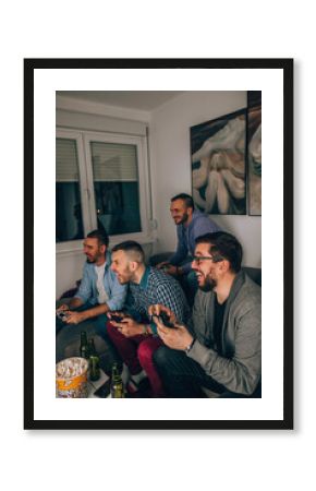 Four happy men playing games and drinking beer while sitting on sofa.