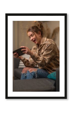 A cute girl gamer in youth clothes has fun playing mobile games on a portable game console remotely with friends. Funny adventure video games, youth culture, virtual reality, modern technologies.