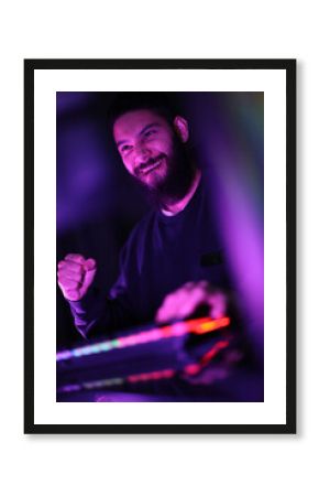 vertical photo A young man plays a computer game in a room with colorful neon lights. raising fists merrily with satisfaction in the black studio A man wearing headphones intends to play a game online