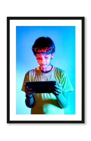 Boy playing videogame on tablet in room with neon inscription