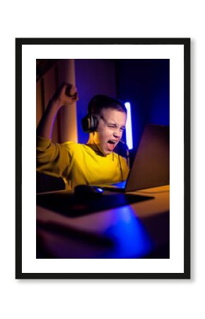 Young excited boy gamer with headphone playing video game on laptop at home.