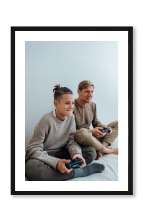 Teenager boy having fun enjoying play console video game with father while sitting on bed at home.