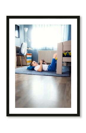 Boy playing video game on smartphone laying on floor in his room.