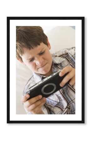 Young boy with handheld game indoors looking unhappy