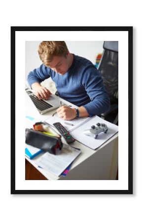 Teenage Boy Studying In Bedroom Using Laptop