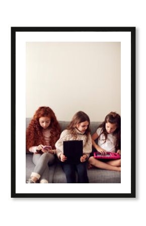 Group Of Girls With Friends Sitting On Sofa At Home Playing On Digital Tablet And Mobile Phones