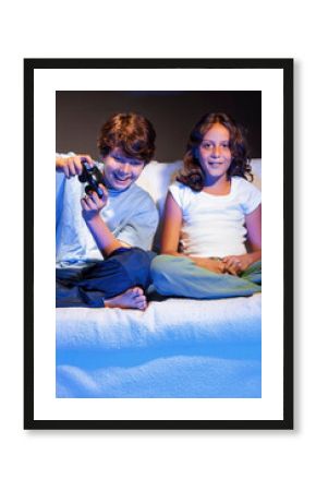 Two young children playing video games at night on the sofa