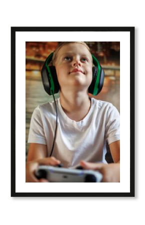  Boy in white t-shirt and gaming headphones plays video game with wireless controller. Concept of games, children and technology, screen time and home leisure.