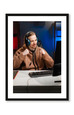 male gamer in headphones shaking fists gesturing yes and shouting play video game online in neon light at night. Gaming at Home. Online Multiplayer Championship. Esport streaming game.