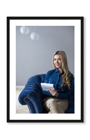 Beautiful female psychologist or consultant posing with a clipboard in a therapeutic office smiling, wearing a blue shirt and sitting in a chair.