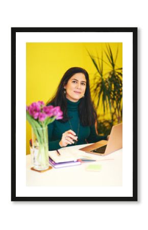 Beautiful middle age woman working in colorful cosy office, using portable laptop computer