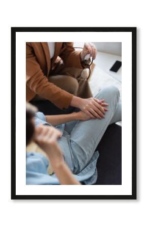 cropped view of psychologist holding hand of depressed patient, blurred foreground