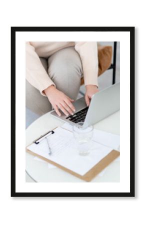 Close-up of women's hands typing using a laptop. The concept of online learning. The work of a psychotherapist online. There is a glass of water and a clipboard on the table.