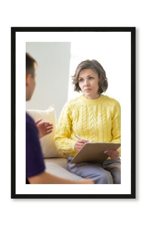 Woman psychologist in a chunky-knit sweater listens attentively to a teenage boy. Blurred foreground.