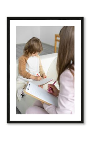 Little boy psychologist's appointment. He draws  picture of his family request of  psychologist. An unrecognizable psychologist analyzes drawing and makes notes for himself. Blurred foreground.