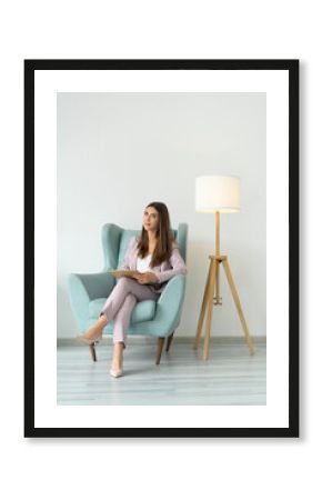 Female psychologist in a dusty pink suit in a cozy chair next to a floor lamp. Looks into the camera. mental health.