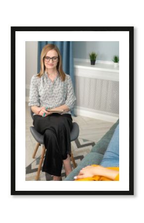 Female psychologist in glasses, blouse and black trousers conducts a psychological session in her office with a young woman lying on the couch. At a psychotherapist's appointment. Vertical photo