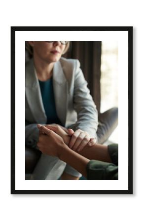 Close-up of experienced psychologist keeping hand on those of young depressed female patient while comforting her during session