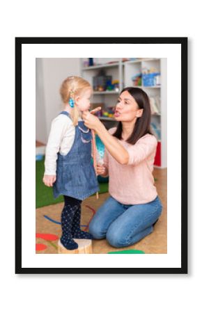 Woman speech therapist helps cute girl to learn correct pronunciation and literate speech