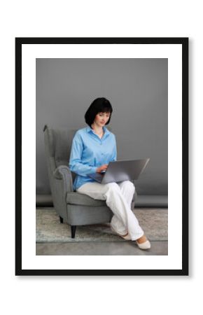 Positive adult business woman mentor teacher psychologist sits on armchair consulates talk in online seminar on laptop, work with patients at home in remote, teach advice by digital training at office