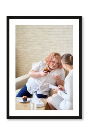 Obese young woman enjoying delicious cupcakes and smiling while having therapy session with highly professional psychologist