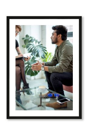 Female psychologist consulting indian man, writing notes during psychological therapy session