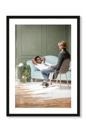 Young afro ethnicity man having a serious conversation with psychologist lying on the comfortable couch during psychological session in the office. Image with copy sopce