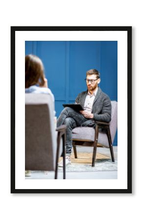 Handsome male psychologist listening to the woman client sitting during psychological session in the blue office interior