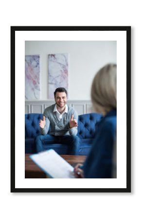 Man sits on the couch smiling and talking to a psychologist consultant.