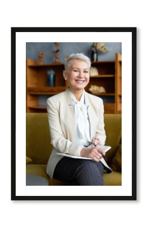 People, age, career, profession and occupation concept. Vertical shot of cheerful mature woman entrepreneur having great idea, making plan or strategy for company, writing down in notebook, smiling