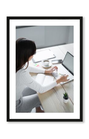 Business woman in glasses sits table and types on laptop holding pen in her hand.
