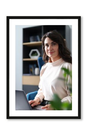 A woman is sitting in front of a laptop computer. She is wearing a white shirt and has long hair