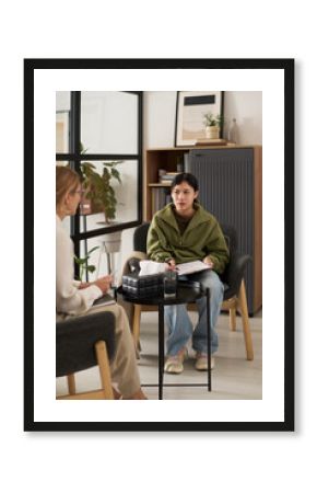 Vertical full length portrait of teenage girl signing consent form on clipboard during therapy session with female psychologist