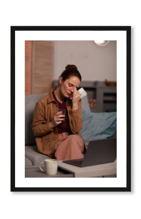 Depressed young woman crying while sitting on sofa and talking online on laptop with her psychologist