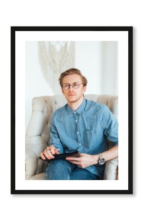 Portrait of serious caucasian man psychologist sitting in armchair at the workplace, holding a folder with papers for notes.