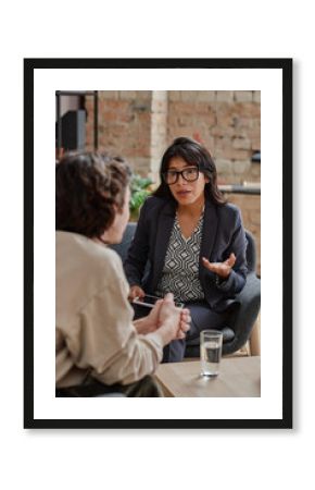 Vertical medium shot of unrecognizable young man treating depression with help of professional psychotherapist listening to her suggestions