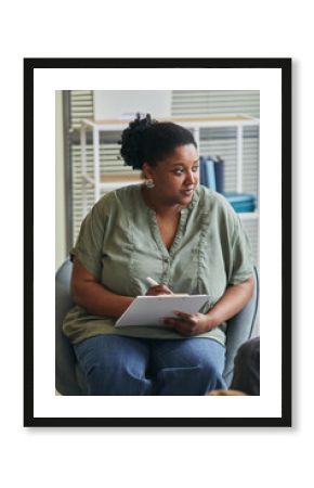 African young psychotherapist sitting on chair and making notes during session with her patient