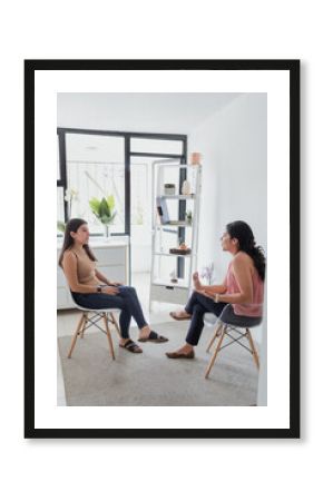 Hispanic young woman psychologist and female patient telling about mental problems while doctor is listening and making notes. Psychotherapy concept in Mexico Latin America 